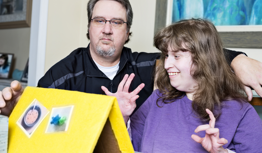 Disabled girl smiles as she participates in speech therapy at home with her Dad. She is nonverbal so she communicates what she wants with picture cards.